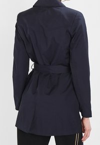 Námořnický trench coat s opaskem, límečkem, dlouhými rukávy a zúženým pasem. Hladká látka s propracovaným střihem a detailem rozparku na zadní straně.
