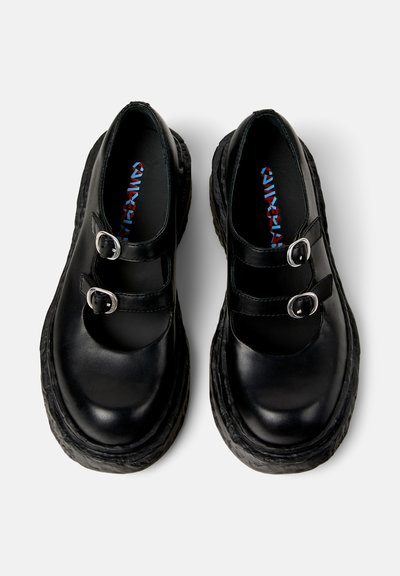Zapatos de cuero negro con correas de doble hebilla, puntera redonda y suela gruesa y texturizada. El interior cuenta con una plantilla de marca colorida.