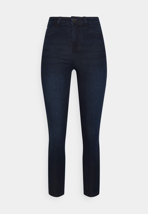 Mørkeblå højttaljede skinny jeans med knapper foran, lynlås og fem-lomme design mod en lys baggrund.