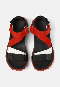 Černé sandály s červenými a bílými pásky, které mají texturovanou podrážku, nastavitelné popruhy a zaoblený design pro bezpečné uchycení.