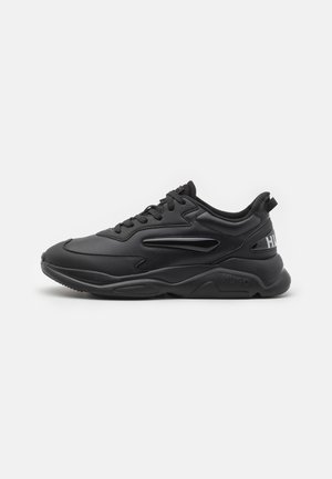 Czarny masywny sneaker z grubą podeszwą, sznurowany z przodu, z wyściełanym kołnierzem wokół kostki i subtelnym detalem logo na pięcie i boku.