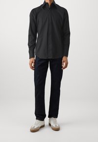 Černá košile s dlouhými rukávy a rozšířeným límečkem, spárovaná s tmavými džíny a bílými teniskami s hnědými akcenty.