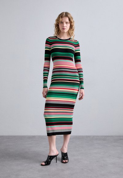 Rochie striată, ajustată pe corp, cu mâneci lungi; culorile includ verde, roșu, negru și galben. Purtați cu pantofi cu toc negri.