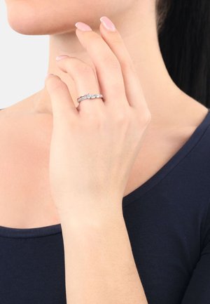 Anello d'argento con un design intrecciato, caratterizzato da piccole pietre incassate. Indossato su una mano, mette in mostra una finitura pulita e lucida.