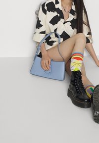 Borsa strutturata azzurro chiaro con manico superiore, abbinata a stivali neri stringati e calzini multicolori a rombi. Camicia con motivo bianco e nero.