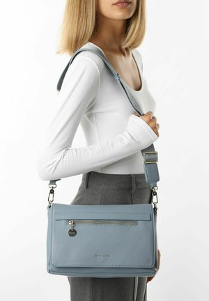 Sac à main en cuir bleu clair à la finition texturée, avec une poche zippée à l'avant, une sangle réglable et des accents métalliques.