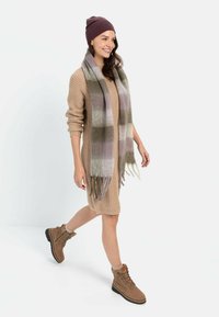 Beige Strickkleid mit langen Ärmeln, kariertem Schal in Grün und Lila, braunen Schnür-Ankleboots mit schwarzen Sohlen.