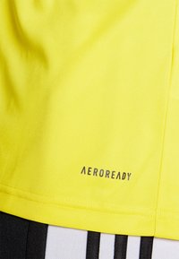 Bright yellow athletic shirt with smooth texture, featuring "AEROREADY" printed in gray, showcased against black and white striped shorts.