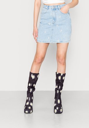 Lyseblå denim mininederdel med blomsterbroderi, kombineret med sorte knæhøje støvler med blomstermønster og plateau såler.