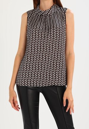 Mouwloze zwart-wit blouse met geometrisch patroon en geplooide halslijn, gecombineerd met zwarte nauwsluitende leren broek.