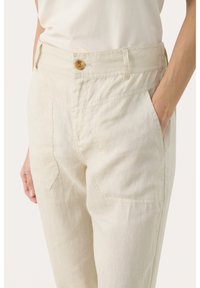 Jasno beżowe lniane spodnie z wysokim stanem, zapinane na guzik, z bocznymi kieszeniami oraz skośnymi tylkami, zapewniające swobodny krój.
