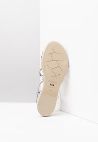 Sandale en cuir argenté avec une semelle beige clair, dotée d'une texture antidérapante et de brides de cheville réglables. Taille 37, marquée "Fabriqué en Italie."