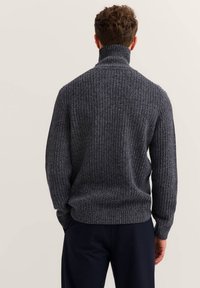 Dunkelgrauer Strickpullover mit hohem Kragen, gerippter Textur und langen Ärmeln, der einen lässigen Schnitt und dezente Details auf der Rückseite aufweist.