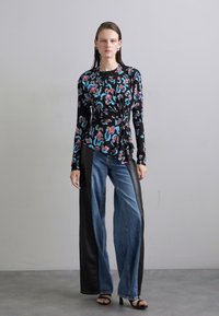 Black long-sleeve top with colorful abstract print, paired with wide-leg denim jeans featuring leather side panels. Black heels complete the look.