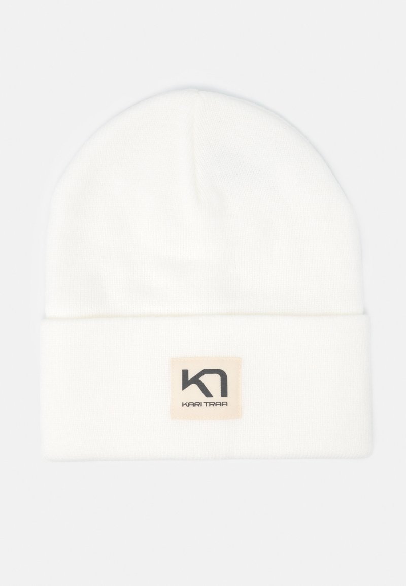 Witte gebreide beanie met een opgerolde rand, voorzien van een rechthoekige beige patch met zwarte logo-tekst. Zachte textuur en warm ontwerp.