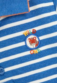 Modrá a biela pruhovaná polo košeľa s farebnou vyšívanou nášivkou s tvárou leva a textom "WILD ONE." Gombíkový detail na golieri.