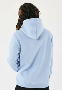 Felpa leggera blu chiaro realizzata in un tessuto morbido e elastico. Presenta un cappuccio con cordino e polsini a costine con una vestibilità comoda. Linee semplici e texture liscia.