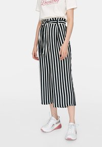 Culottes rayées noir et blanc avec une ceinture nouée, présentant un design à jambe large et un tissu lisse. Associées à des baskets blanches.