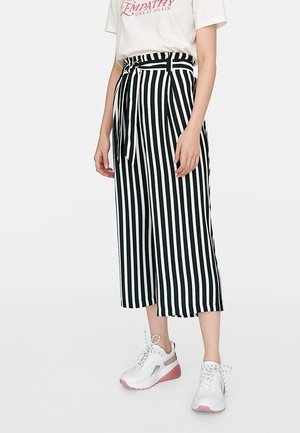 Culottes rayées noir et blanc avec une ceinture nouée, présentant un design à jambe large et un tissu lisse. Associées à des baskets blanches.