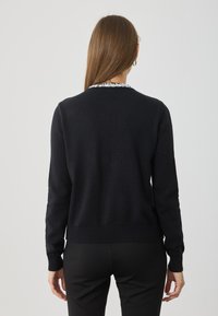 Czarny sweter z dzianiny z ściągaczem u dołu i na mankietach, z teksturowanym srebrnym detalem przy dekolcie. Prosty i dopasowany fason.