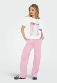 White t-shirt with a colorful "Havana" graphic, paired with loose, light pink trousers and blue sneakers with white accents.