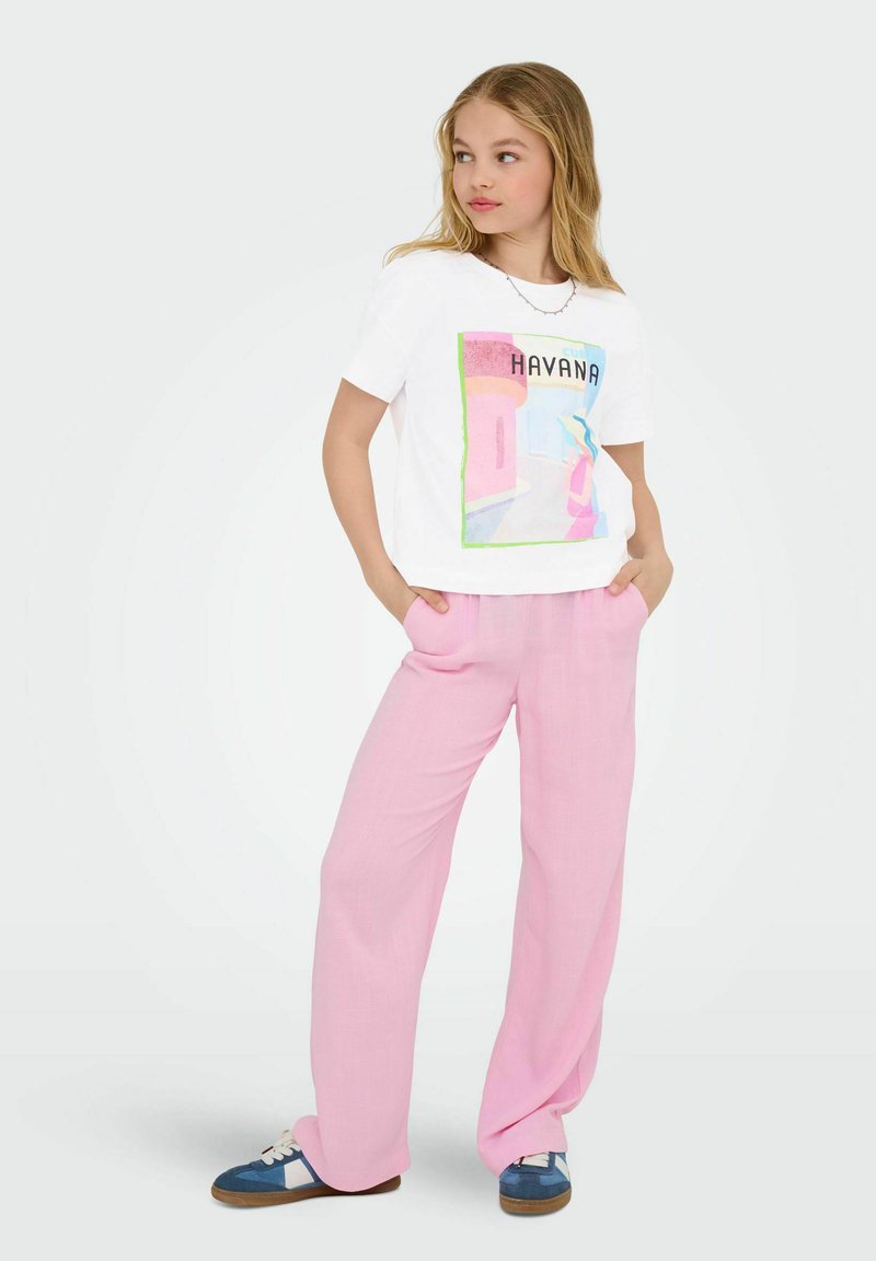 White t-shirt with a colorful "Havana" graphic, paired with loose, light pink trousers and blue sneakers with white accents.