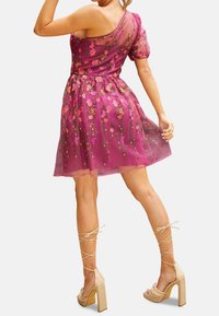 Kukkaprintillä varustettu vaaleanpunainen läpikuultava mekko, jossa on liehukevyiset hihat ja istuva vyötärö. Yhdistetty beigen värisiin korokepohjakenkiin, joissa on ristikkäiset nauhat.