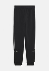 Svarta sportbyxor med grå sidostrippar, resårmidja och ribbade muddar; har präglad logotypdetalj nära ankeln.