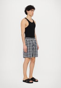 Svart tanktopp kombinert med marineblå og hvit rutete bad shorts. Har elastisk midje og svarte sandaler som kan glides på.