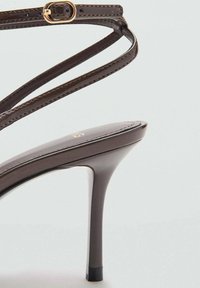 Braune Sandale mit hohem Absatz, dünnen Riemen mit Schnalle, glatter Oberfläche, spitzer Zehenpartie und Stiletto-Absatz.