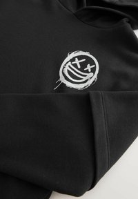 Black sweatshirt made of soft fabric featuring a white graphic of a smiling face with Xs for eyes. Accented details include stitching along the seam.