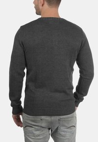 Maglione grigio lavorato a maglia con scollo rotondo, polsini e orlo a costine, e una finitura testurizzata. La vista dal retro mostra una silhouette aderente.
