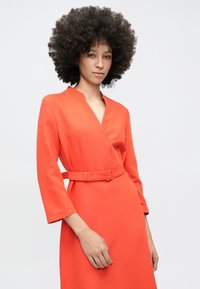 Oranž wrap-kleit sügava V-kaelusega, pikkade varrukatega ja vöökohal sobiva pandla vöögiga. Sile kangas puhta ja peene disainiga.