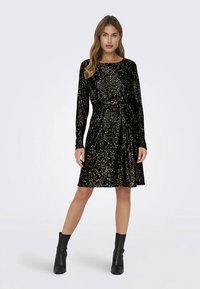 Czarna sukienka z aksamitu z długimi rękawami, z paskiem w talii i teksturowaną powierzchnią ozdobioną błyszczącymi cekinami. Długość do kolan.