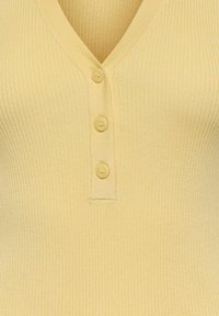 Gros plan sur un haut tricoté jaune clair à côtes avec col en V et trois petits boutons assortis alignés au centre devant.