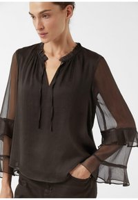 Zwarte, lichtgewicht blouse met een gerimpelde halslijn en strikdetail; doorschijnende, uitlopende mouwen met gelaagde ruches; gladde textuur.