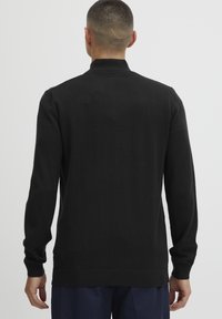 Black knit sweater with a high collar, long sleeves, and ribbed cuffs. Soft texture and fitted design with a straight hem at the waist.