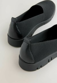 Czarne buty wsuwane z teksturowanej siateczki, gładką kontrą piętową oraz grubymi gumowymi podeszwami z rowkami bieżnika na jasnej powierzchni.