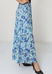 Jupe maxi florale avec un motif bleu et blanc, dotée d'un design à niveaux et d'une taille élastique pour le confort. Texture satinée.