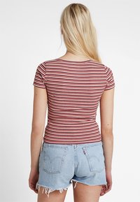 Krótki rękaw, dopasowany top w czerwono-białe poziome paski, zestawiony z jasnoniebieskimi szortami dżinsowymi z postrzępionymi brzegami i tylnymi kieszeniami.