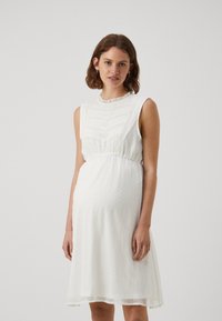 Robe blanche sans manches en tissu texturé à pois, avec un col froncé et une taille élastique, arrivant juste au-dessus du genou.