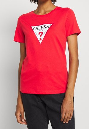 T-shirt en coton rouge à manches courtes et encolure ras du cou ; présente un graphique triangulaire blanc avec les mots "GUESS" et un point d'interrogation.