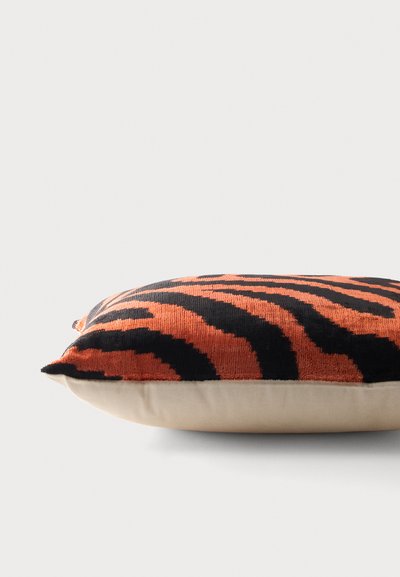 Coussin rectangulaire avec une base beige et un dessus en tissu texturé présentant un motif à rayures de tigre noir et orange, reposant sur une surface plane.