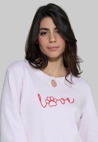 Felpa lilla chiaro con scollatura a chiave, decorata con il testo rosso "amore" e un'impronta di zampa. Tessuto morbido con una vestibilità comoda.