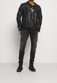 Svart lädermotorcykeljacka med dragkedja framtill och strukturerade ärmar, kombinerad med åtsittande svarta jeans och svarta sneakers.