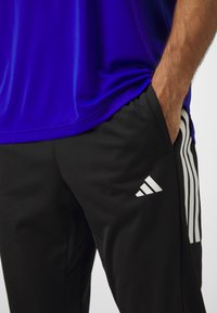 Adidas träningsset bestående av en klarblå tröja och svarta byxor med vita ränder och logotyp, tillverkade av mjukt och lätt material.