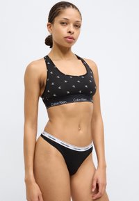 Μαύρο αθλητικό σουτιέν και στρινγκ με ολόκληρο το μοτίβο λογότυπου CK. Απαλό ύφασμα, χοντρές τιράντες με την επωνυμία Calvin Klein. Σχεδιασμός racerback.