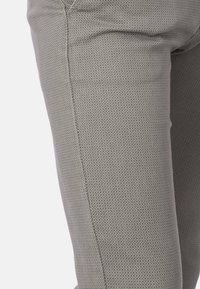 Pantaloni grigi con texture che presentano un motivo geometrico, taglio slim e cuciture visibili lungo la cucitura laterale. Il materiale appare liscio e resistente.