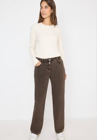 Pantaloni larghi marroni con due bottoni, tasche laterali e una consistenza morbida. Abbinati a un maglione crema e sneakers bianche.