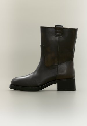 Bottine en cuir marron foncé, à bout arrondi, avec des surpiqûres sur le panneau latéral, une tirette et un talon bloc épais, vue de profil.